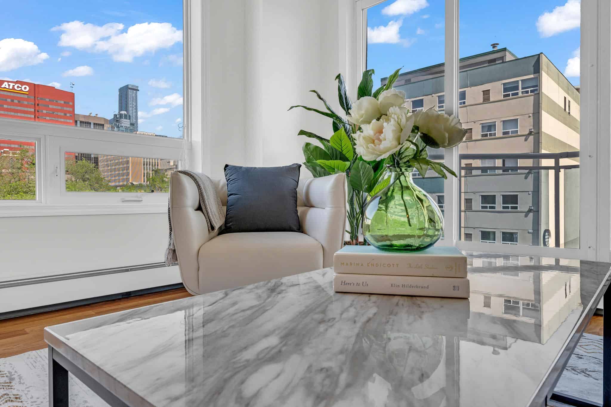 Stuck at 60+ Days? How to Sell Your Edmonton Home Without a Price Drop 1 close up of living room coffee able with vse of flowers and books. arm hair in background with city scape outside windows. stage and style by leigh edmonton ab